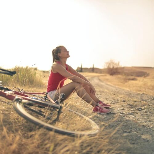 A woman enjoying the sunlight while taking a break from riding her bicycle.